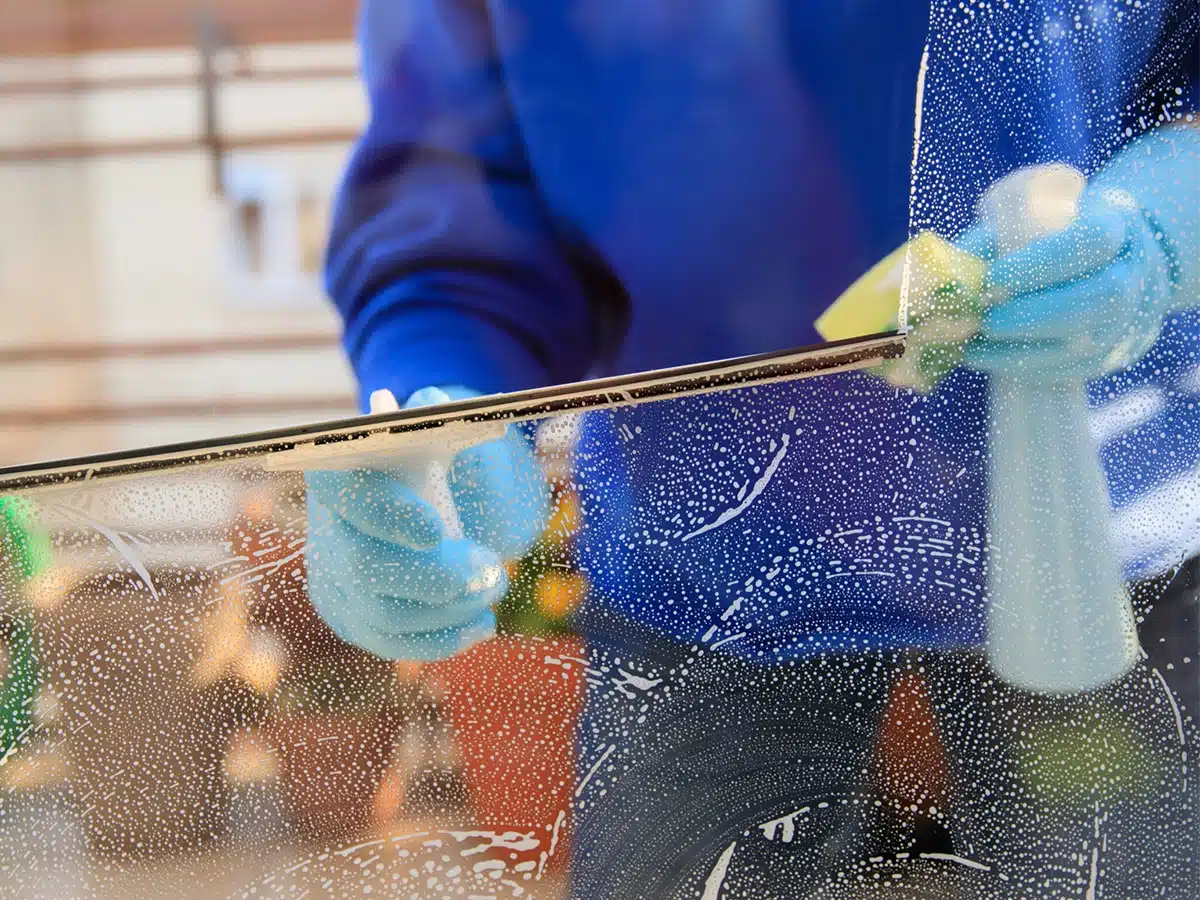 Die Reinigungskraft verwendet Abzieher, Schwamm und Seifenlauge, um ein Fenster zu reinigen.